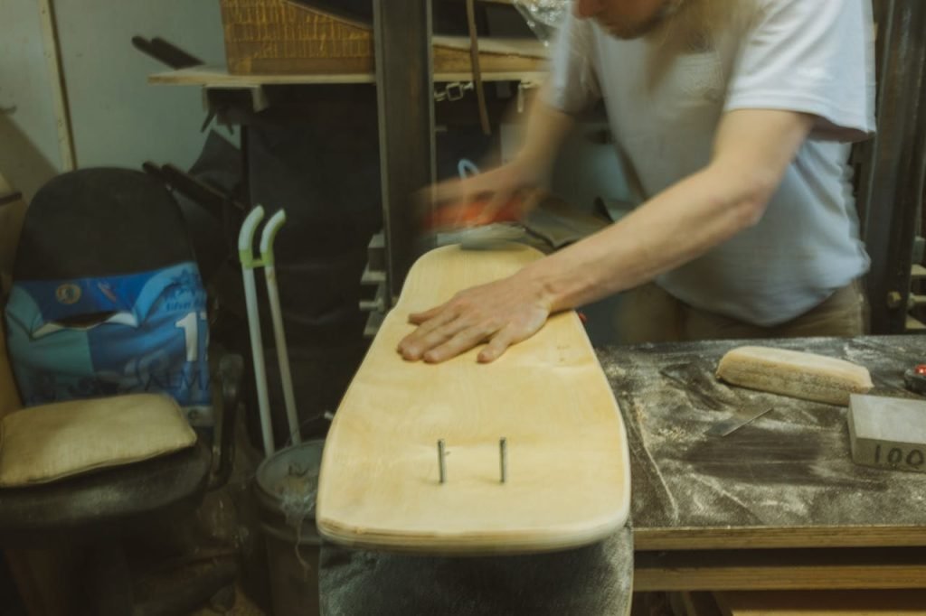 A skilled craftsman shaping a wooden skateboard in a workshop setting.